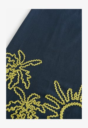Tessuto scuro con complessi ricami in giallo a forma di fiori realizzati con rickrack, contrasto di texture tra lo sfondo liscio e il design in rilievo.