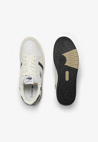 Sneakers Lacoste in pelle bianca con dettagli in suede beige e suola in gomma nera. Presentano punta perforata, colletto imbottito e logo ricamato.