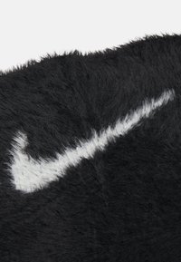 Juodas audinys su ryškiu baltu Nike Swoosh logotipu, padengtas ilgais, švelniais plaukeliais. Išskirtinė monochrominė spalvų gama.