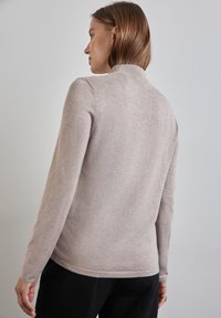 Lichtgrijze, lange mouwen trui met een hoge hals, zachte textuur en ribgebreide accenten bij de kraag en onderkant. Eenvoudig ontwerp aan de achterkant.