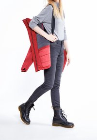 Rød og grå polstret jakke hengende over en grå sweater, parret med sorte skinny jeans og sorte snørebåndsstøvler med gule syninger.