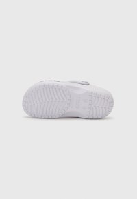 White sneaker with a textured rubber sole, rounded shape, and adjustable strap. Features smooth upper material and embossed logo detail.