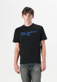 Svart bomull t-skjorte med blå trykt tekst "KARL LAGERFELD JEANS" og sirkel detaljer. Korte ermer, rund hals, klassisk passform.