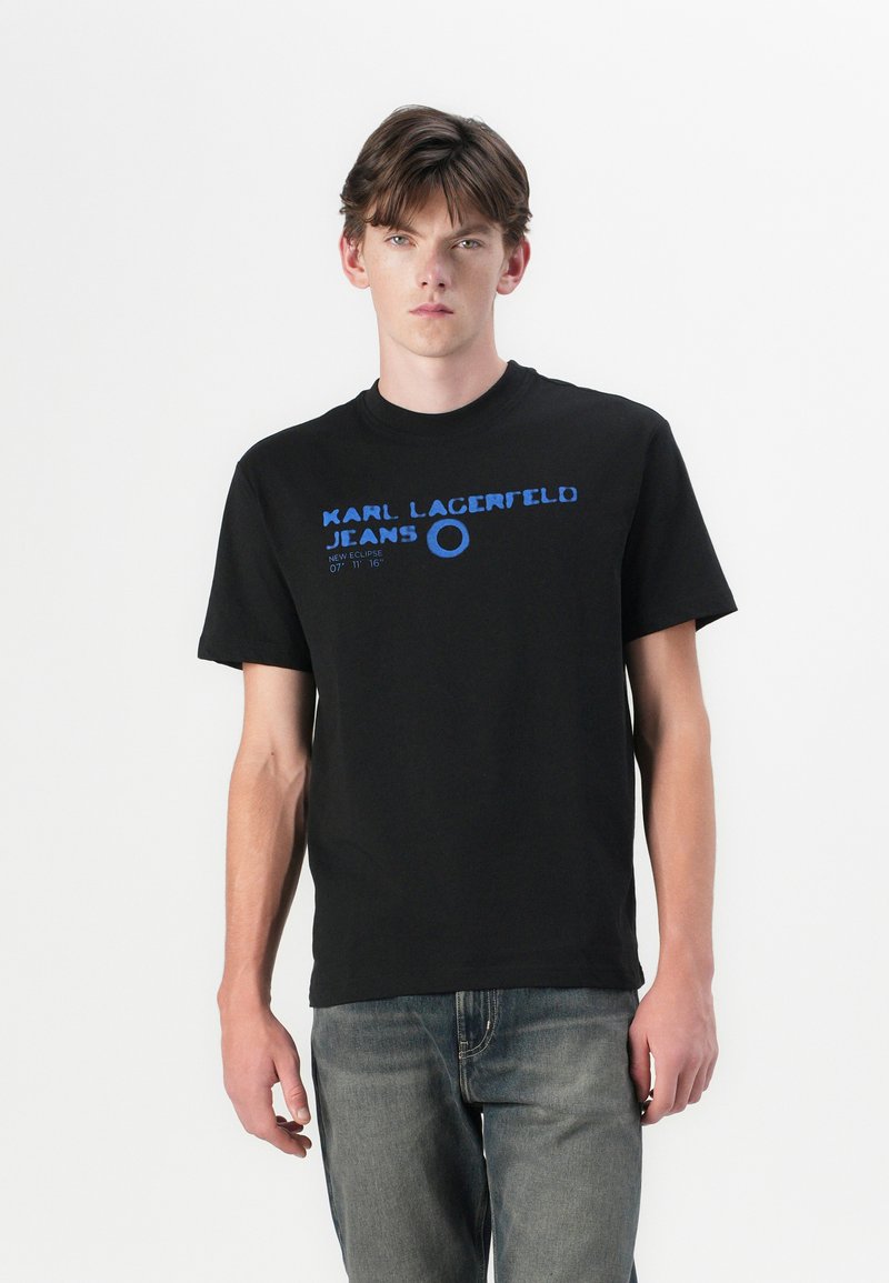 Svart bomull t-skjorte med blå trykt tekst "KARL LAGERFELD JEANS" og sirkel detaljer. Korte ermer, rund hals, klassisk passform.