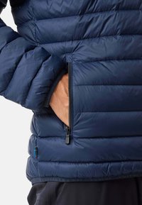 Giacca imbottita blu navy con cuciture orizzontali, dotata di una tasca laterale con zip e un'etichetta in tessuto con accenti blu e gialli sull'orlo.