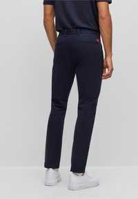 Dunkelblaue Slim-Fit-Hosen mit glatter Textur, elastischem Bund und Gesäßtaschen, kombiniert mit weißen Sneakers mit Logo.