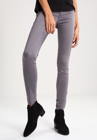 Jeans ajustados grises de denim, con una textura suave y un diseño elegante. Combinados con botas negras hasta el tobillo con un ligero tacón.