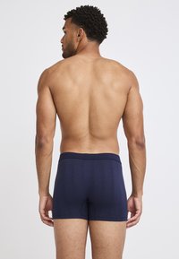 Marinblå boxerkalsonger med en mjuk textur, elastisk midjeband och en åtsittande design, sedd bakifrån.