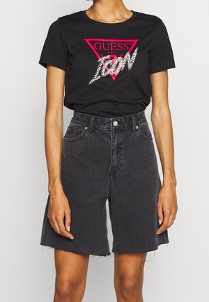 Musta Guessin t-paita, jossa punainen kolmionmuotoinen logo ja teksti "ICON", yhdistetty korkeavyötäröisiin, rispa-reunaisiin mustiin farkkushortseihin.