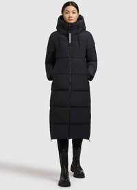 Abrigo puffer largo negro con capucha, que presenta un cierre de cremallera, diseño acolchado y bolsillos laterales. Se lleva sobre leggings negros y botas gruesas.