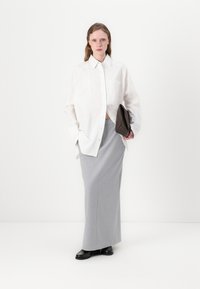 White oversized button-up shirt, grey fitted maxi skirt, black shoes, and a brown clutch; smooth fabrics, relaxed design, clean lines.