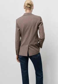 Hnedý sako s vzorom houndstooth, so zapracovaným rozparkom vzadu a klopovými goliermi, skombinované s tmavými džínsami.