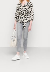 Blusa avvolgente con stampa leopardata in beige e nero, abbinata a jeans grigi slim-fit e sneaker bianchi. Accessorio: piccola borsa beige con maniglie corte.