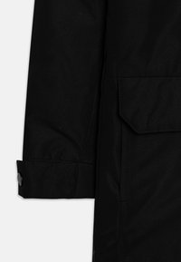 Detalle de una chaqueta negra impermeable que muestra una textura suave, cierre de botón en la manga y un bolsillo de parche en la parte frontal.