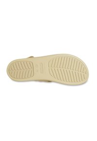 Crocs-skor med en texturerad beige gummisula, med ett mönster av slitbanor och varumärkeslogga inpräntad i mitten.