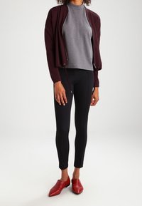 Bordeaux villatakki, harmaa korkeakauluksinen paita, mustat leggingsit ja punaiset kärkipopot. Villatakissa on nyörit; asu yhdistää tiukkoja ja reilumpia tyylejä.