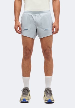 Mann trägt hellgraue Sportshorts, weiße Crew-Socken und graue Laufschuhe mit blauen Akzenten, steht vor weißem Hintergrund.