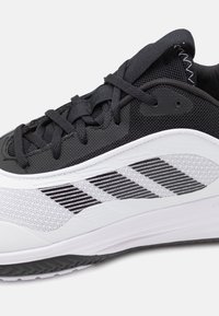Chaussure de sport noire et blanche avec une tige en mesh, des accents texturés et un design rayé sur le côté. Semelle extérieure en caoutchouc avec motif de crampons.