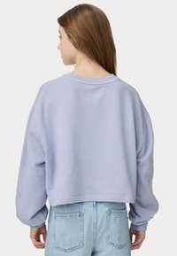 Kortärmad, ljus lavendelfärgad sweatshirt med sänkt axel och ribbad halsringning, i kombination med ljusblå denimjeans med fickor.