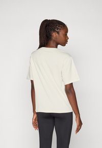 Lichtbeige T-shirt met korte mouwen en ronde hals, met een gladde textuur en een relaxed fit, gedragen met zwarte leggings. Geen bijzonderheden in patronen.