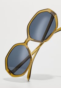 Ochelari de soare octogonali cu rame transparente de culoare muştar şi lentile gri închis. Construcţie din plastic uşor, cu brate elegante.