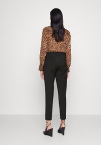Leopardo rašto bluzonas su ilgomis rankovėmis, derinamas su juodomis pritaikytomis kelnėmis ir juodais platforminiais bateliais. Dėmesys tekstūruotam audiniui ir elegantiškai išvaizdai.