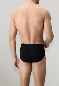 Slip da nuoto neri con una texture liscia ed elastica, caratterizzati da un design a vita bassa e una copertura minimale sul retro. Senza motivi visibili o parti metalliche.