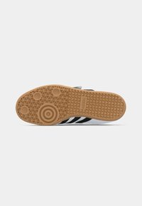 White sneaker sole featuring a rubber gum outsole with circular and diamond patterns, black stripes along the sides, and textured detail.