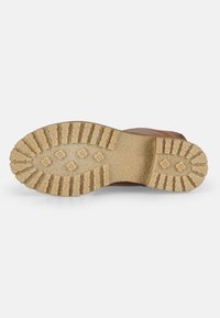 Suela de goma con surcos profundos y una superficie texturizada; color marrón claro; diseñada para tracción y durabilidad; presenta patrones de crestas definidos.