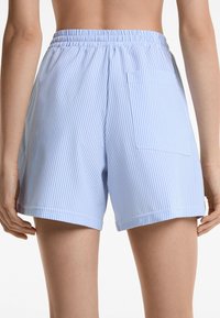 Shorts ray�és bleu et blanc avec une taille élastique, une poche latérale et une coupe décontractée. Tissu en coton avec une texture lisse.