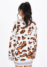 Maglione lavorato a maglia con una base bianca e una stampa leopardata marrone e arancione, polsini a strisce blu e un design rilassato e oversize.
