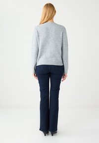 Lichtgrijs, gebreide trui met lange mouwen en een ronde hals, gecombineerd met donkerblauwe wijde jeans. Gladde textuur en een slanke pasvorm.