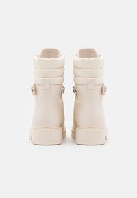 Stivali ankle beige con tomaia trapuntata, colletto arrotondato e fibbie laterali. Realizzati in materiale sintetico con finitura testurizzata. Suola spessa e resistente.