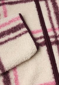 Tissu polaire crème doux avec des rayures à carreaux roses et bordeaux et des finitions bordeaux sur la manche et autour de la fermeture éclair.
