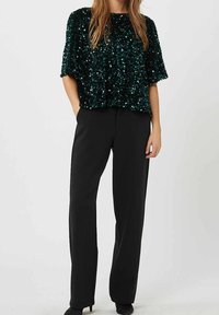 Top verde con paillettes, dalla vestibilità larga e maniche corte, abbinato a pantaloni neri su misura e tacchi a spillo. Tessuto morbido.