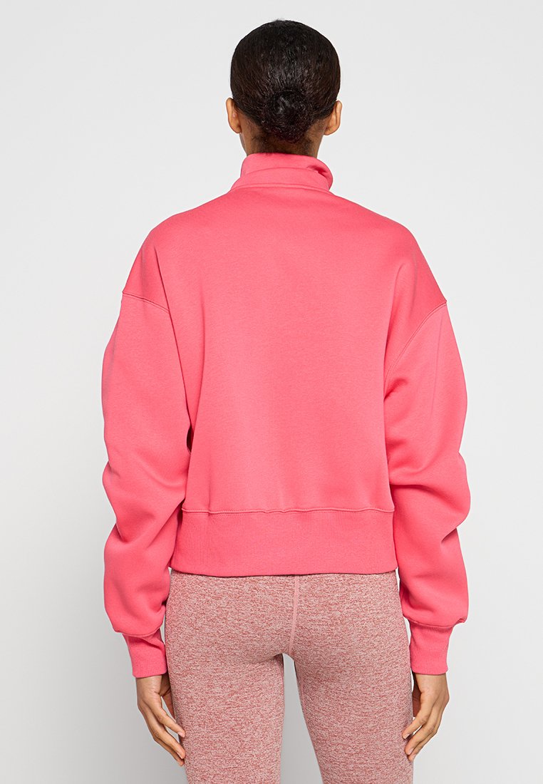 Różowy, oversize'owy sweter z wysokim kołnierzem, ściągaczami na rękawach oraz w pasie. Miękka tkanina, bezszwowe ramiona, noszony z melanżowymi legginsami.