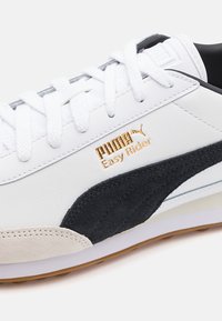 Baskets White Puma Easy Rider avec bande latérale en suède noir, lacets blancs et semelle en gomme, affichant le logo de la marque et les détails de couture.