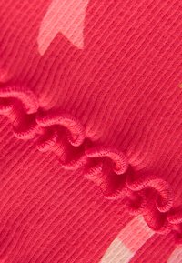 Tissu rose texturé avec un design côtelé, présentant une couture froncée dans une teinte de rose légèrement plus foncée et des motifs abstraits dans des tons plus clairs.