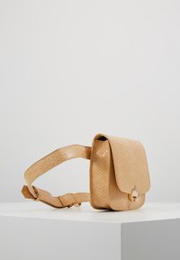 Béžová kabelka přes rameno s texturovaným hadím potiskem. Má klopu se zapínáním na kovový detail a nastavitelný popruh.