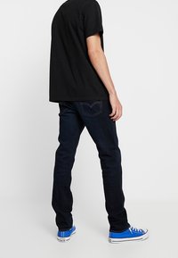 Svart bomulls T-shirt i kombination med mörkblå denimjeans. Varsågod till outfit: avslappnade blå sneakers med vita sulor. Enkel design genomgående.