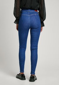 Λεπτά μπλε τζιν από denim, με ψηλή μέση, διακριτικές ραφές και μιας πίσω τσέπη. Φοριούνται με μια μαύρη, υφασμάτινη μπλούζα.