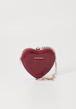 Petit porte-monnaie rouge en forme de cœur avec motifs en relief, fermeture éclair dorée et chaîne dorée attachée avec porte-clés, marqué "GUESS" à l'avant.