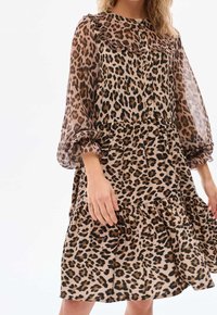 Robe à imprimé léopard en tissu léger et transparent. Dotée de manches longues bouffantes, d'une fermeture à boutons sur le devant et d'un ourlet à volants à étages.