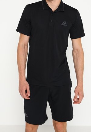 Polo noir à manches courtes et col, avec un logo discret sur la poitrine gauche. Associé à un short noir, le tout en tissu lisse.