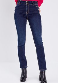 Jean en denim bleu foncé taille haute, ajusté, avec des boutons sur le côté, des coutures contrastées et un design classique à cinq poches.