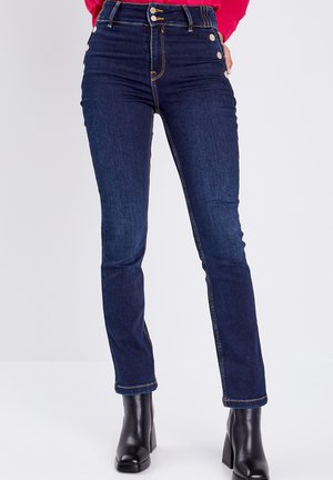 Jeans de mezclilla oscuros de tiro alto y corte ajustado, con botones laterales, costuras en contraste y un diseño clásico de cinco bolsillos.
