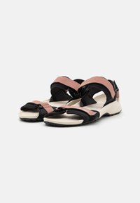 Sorte svarte og rosa sandaler med justerbare stropper, en polstret såle og teksturert grep. Sidevinkelen viser stroppedesignet og materialkontrasten.