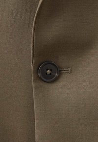 Maslinasto zelena tkanina glatke teksture, s crnim dugmetom s četiri rupe zašivenim na lijevoj strani, naglašena blago izbočenim reverom.