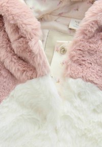 Material moale din blană artificială roz, cu o secțiune inferioară albă, care dezvăluie o căptușeală cu un model floral. Prins cu un nasture cu clip metalic argintiu.