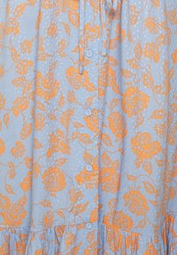 Robe bleu clair avec un motif floral orange, boutons courts et ourlet volanté. Tissu texturé avec des points en relief sur toute sa surface.